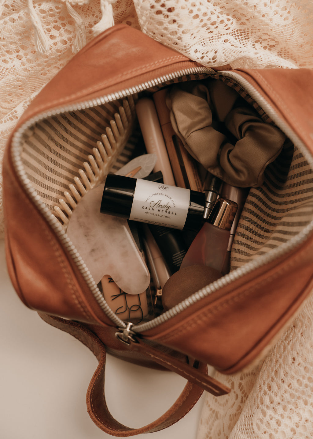 Open brown leather bag with beauty products on a textured beige background