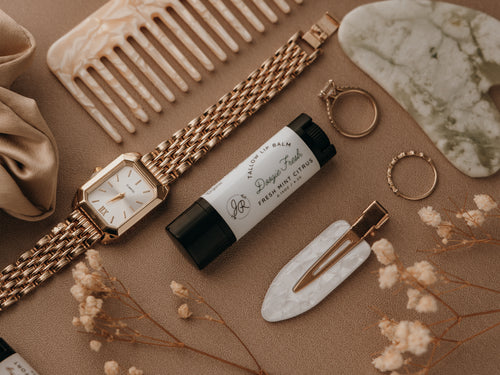 Rose gold watch, hairbrush, and other accessories on a textured surface with flowers.