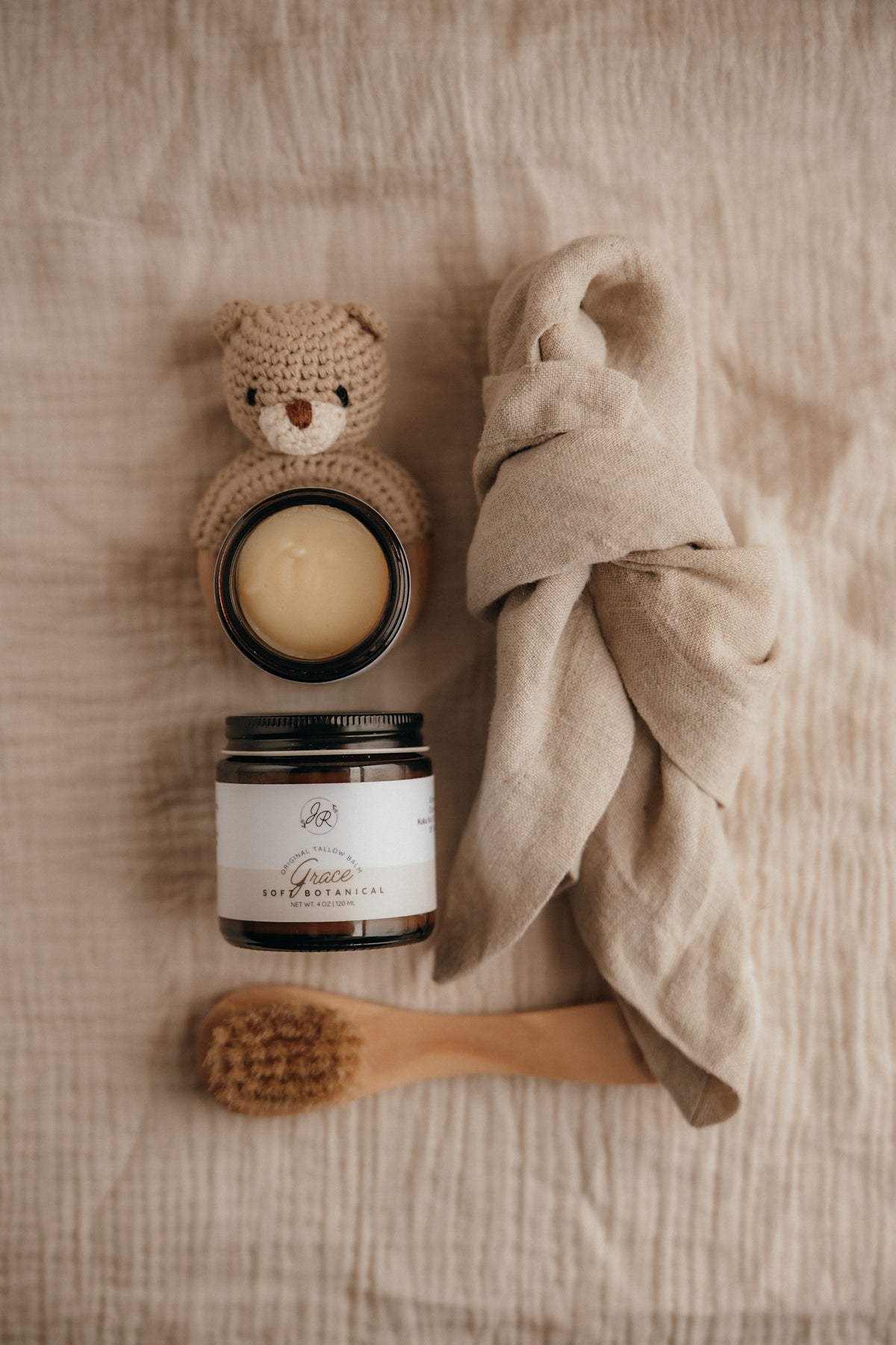 Cosmetic products including a jar, a candle, a towel, and a brush on a textured surface.