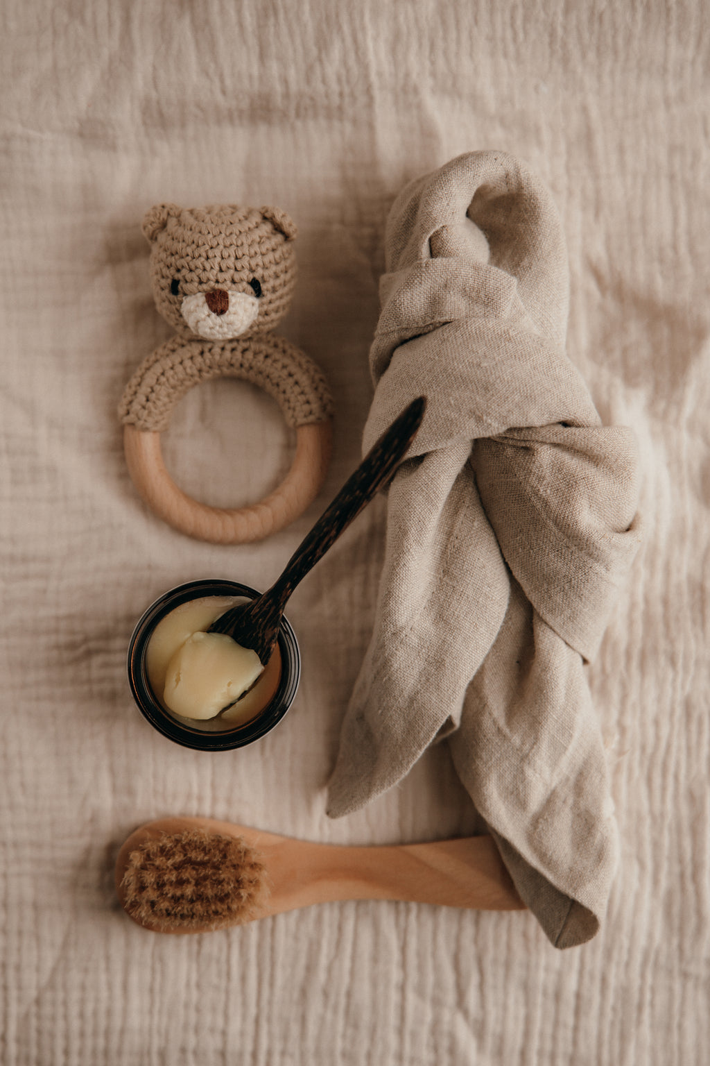Baby care items including a teething ring, towel, bowl with spoon, and brush on a textured surface.