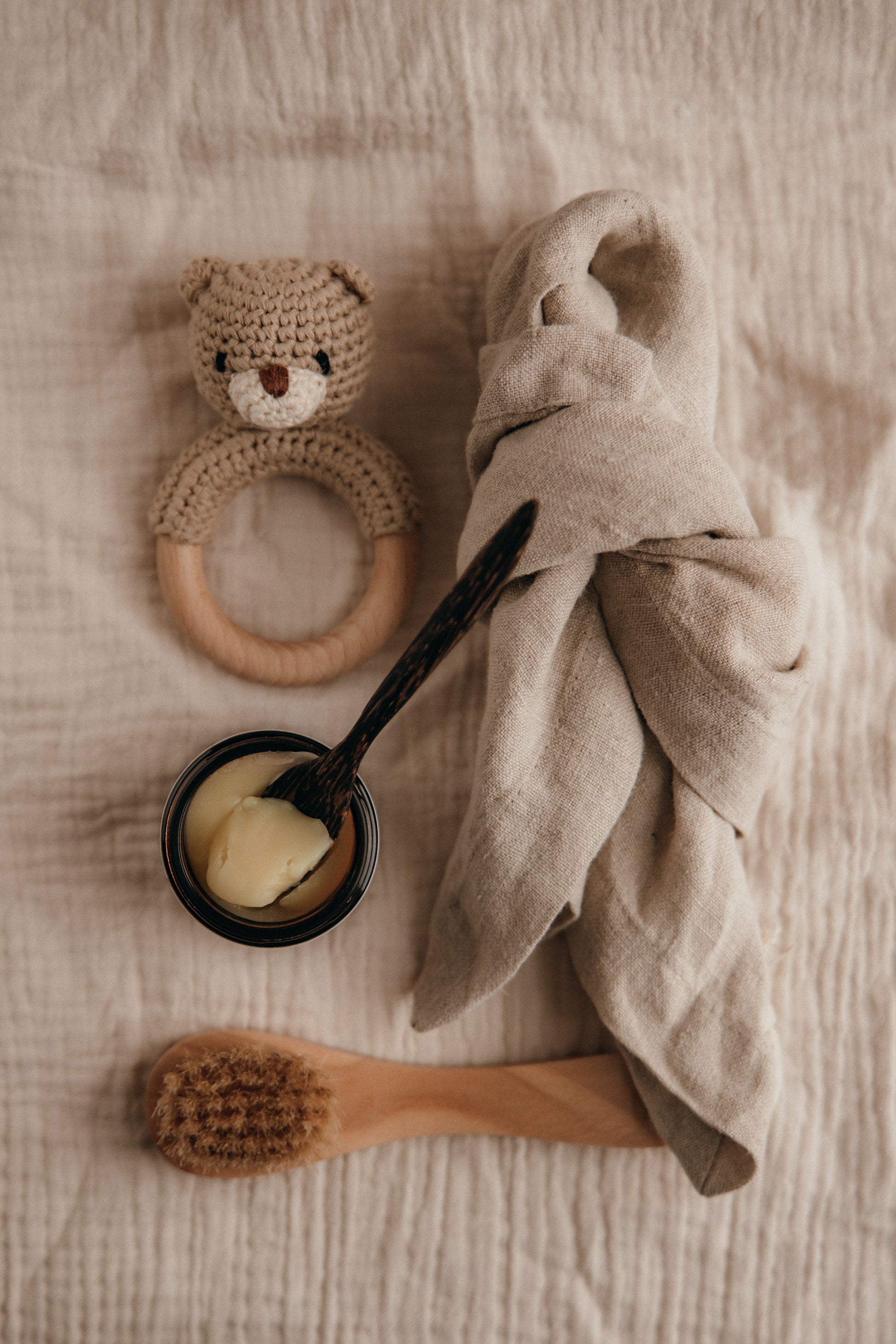 Baby care items including a teething ring, towel, bowl with spoon, and brush on a textured surface.