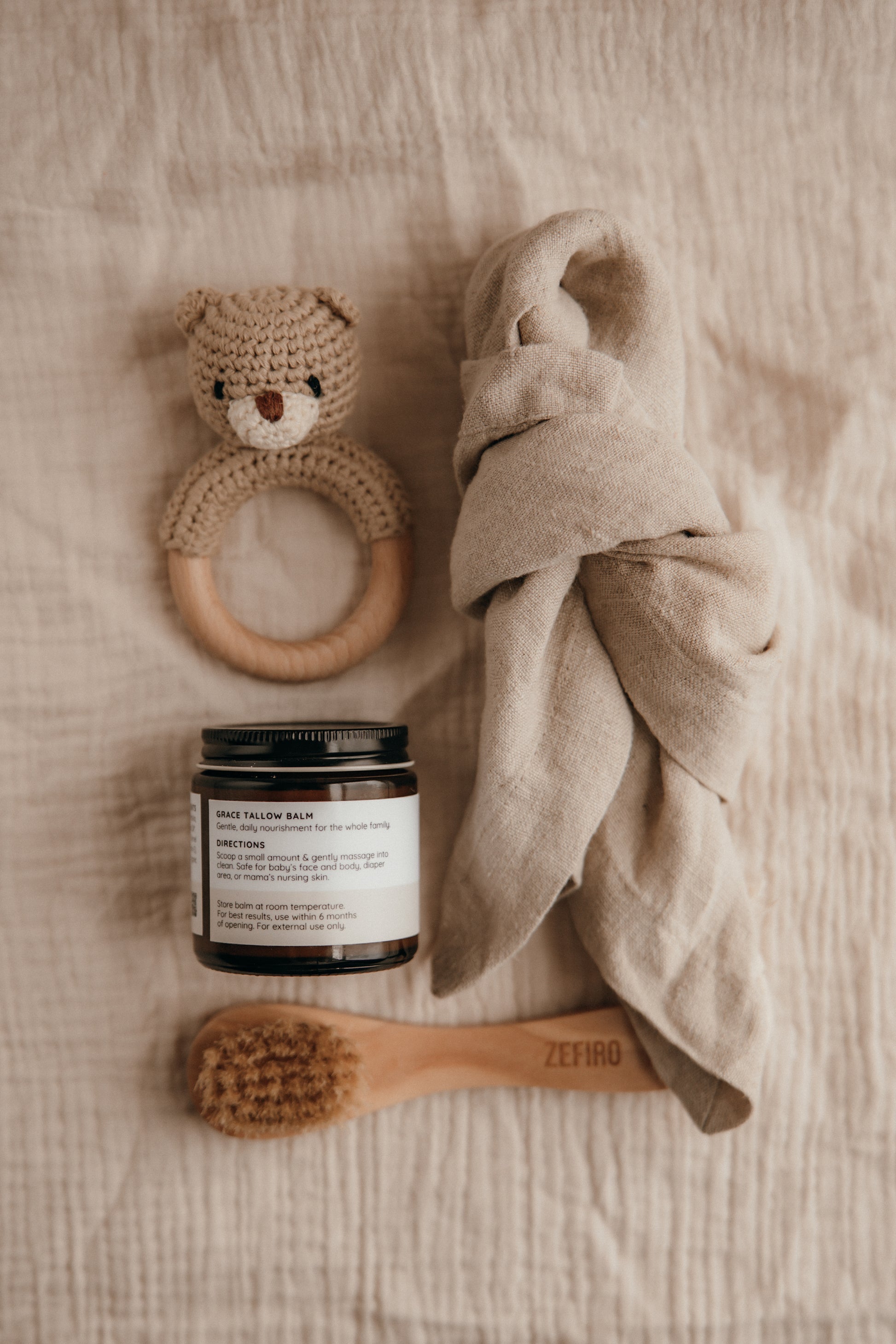 Baby care items including a wooden ring, jar, towel, and brush on a textured surface.