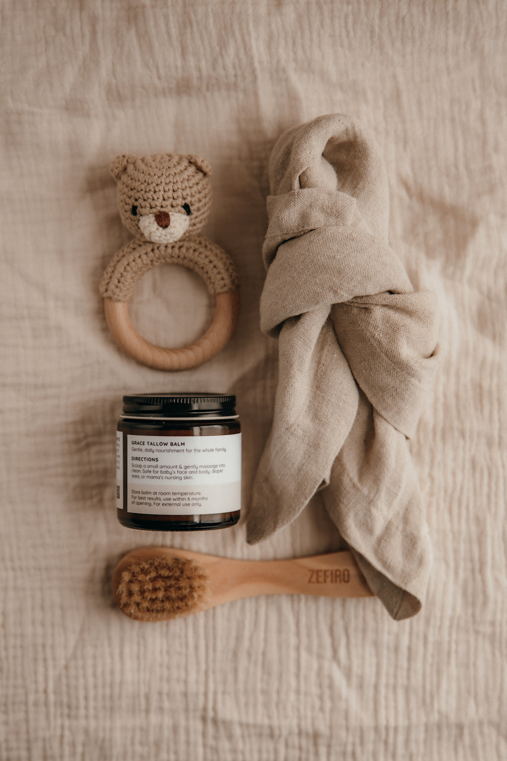 Baby care items including a teething ring, jar, towel, and brush on a textured surface.