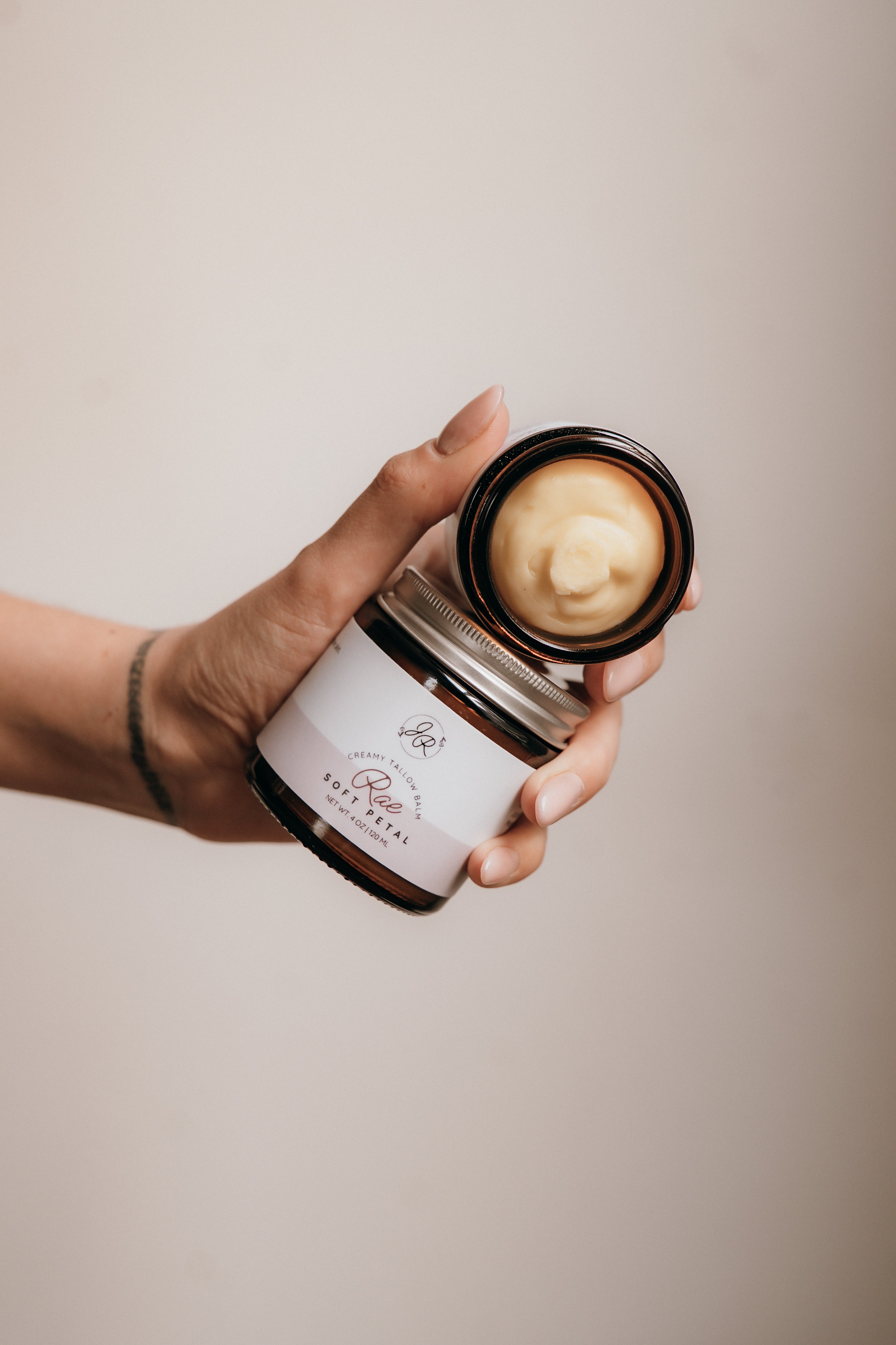 Hand holding a jar of cream with a visible brand name against a neutral background