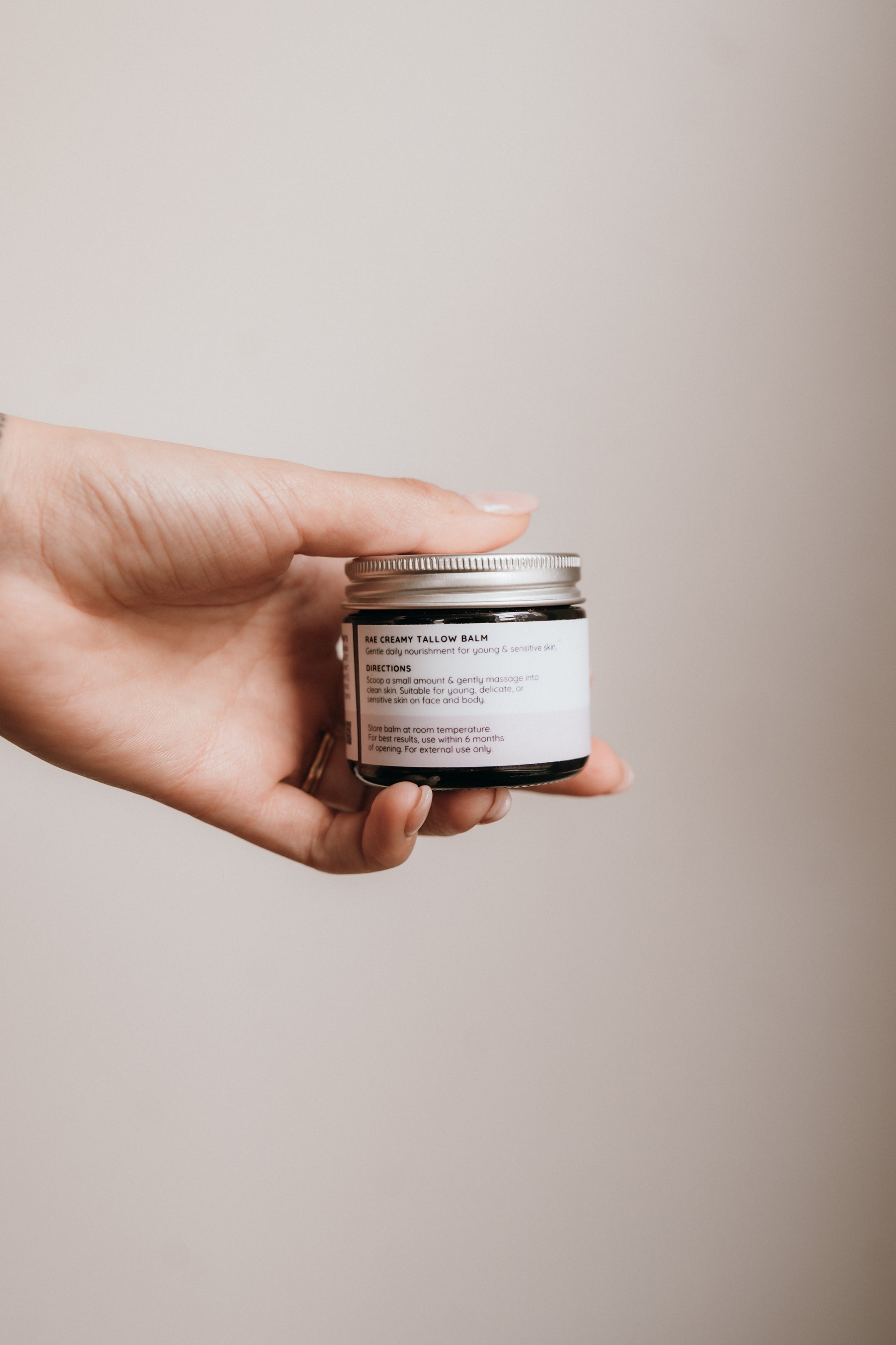 Hand holding a small jar with a label against a plain background