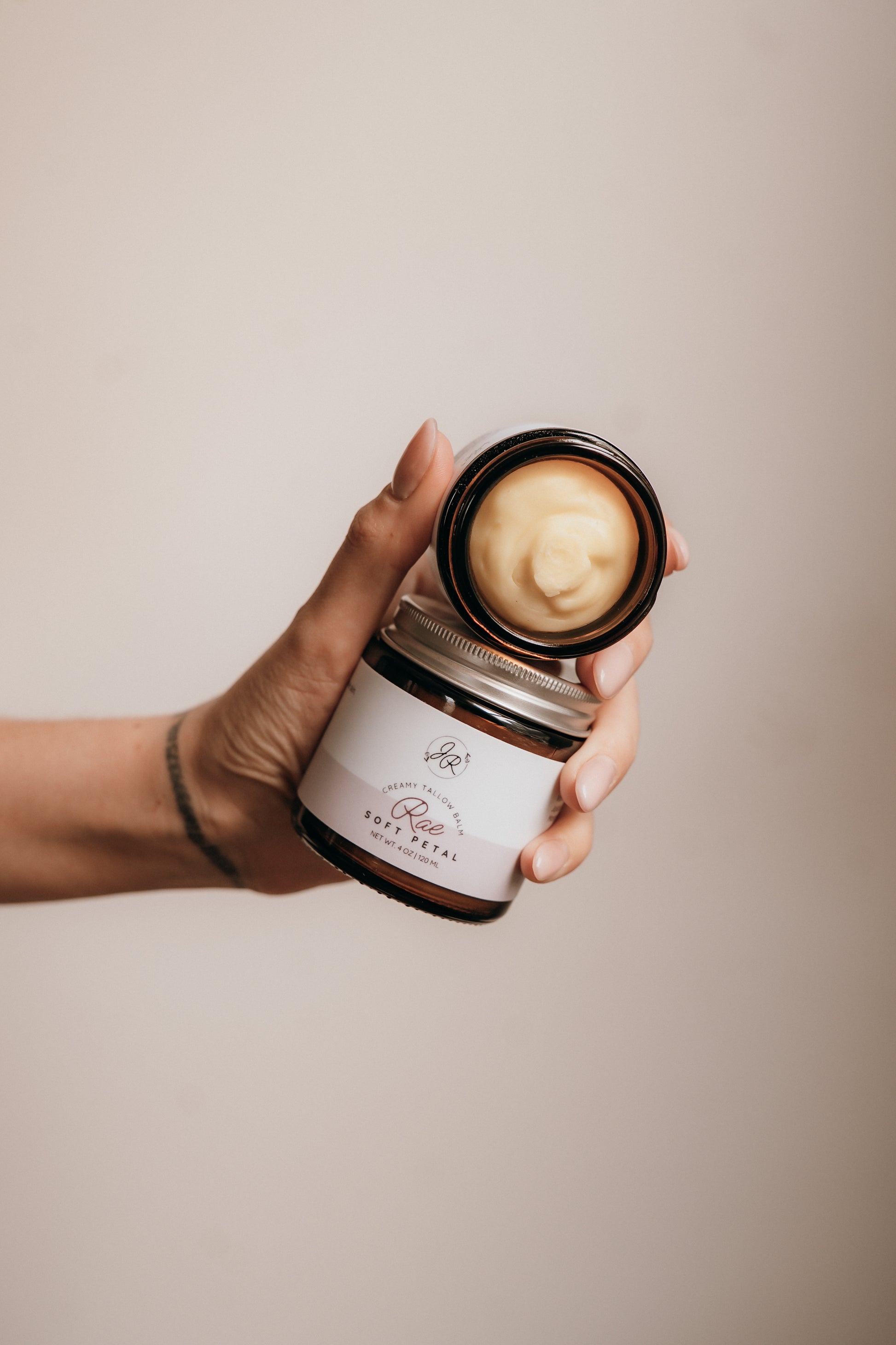 Hand holding a jar of cream with a visible brand label against a neutral background