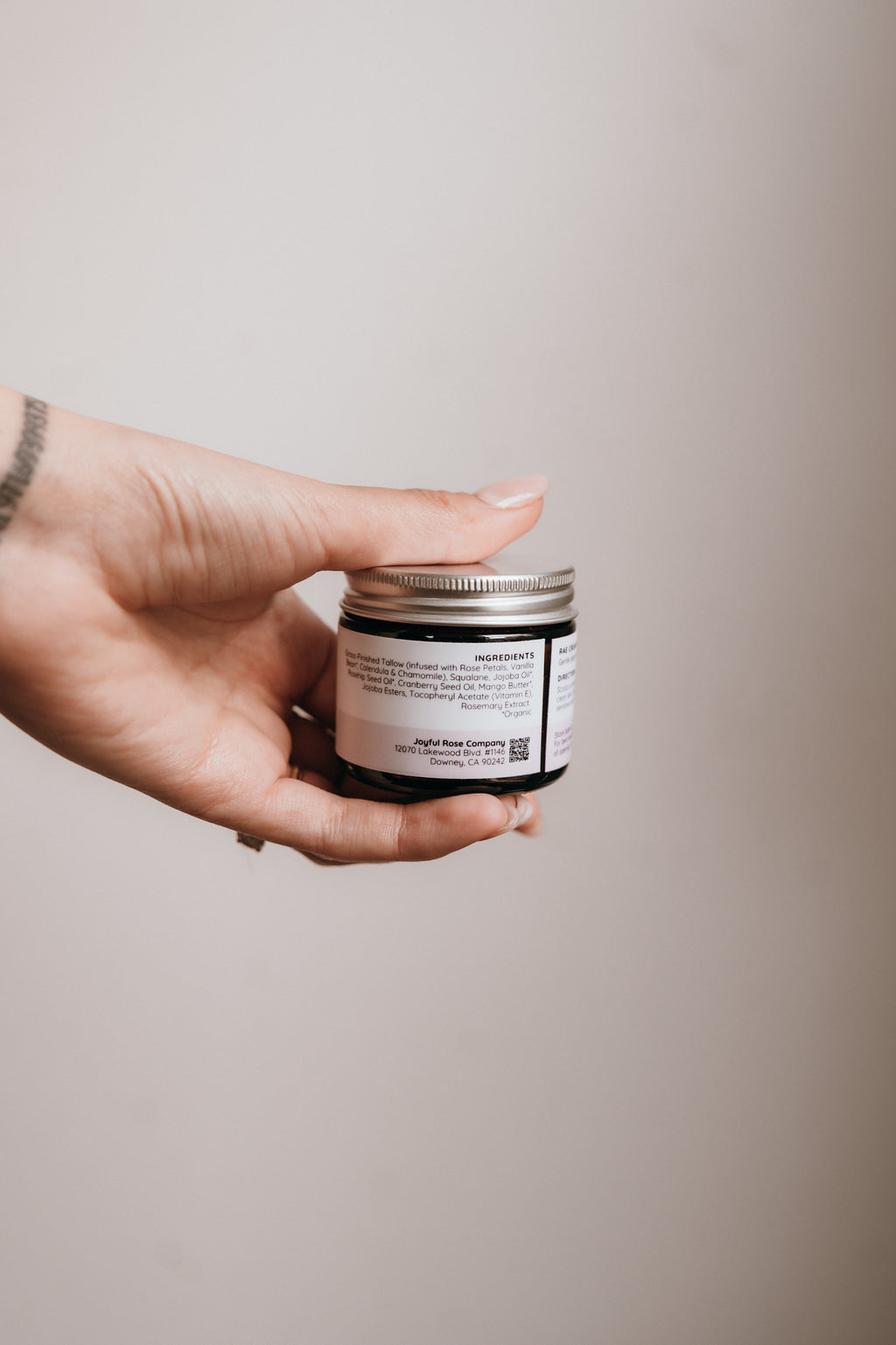 Hand holding a small jar with a label against a plain background
