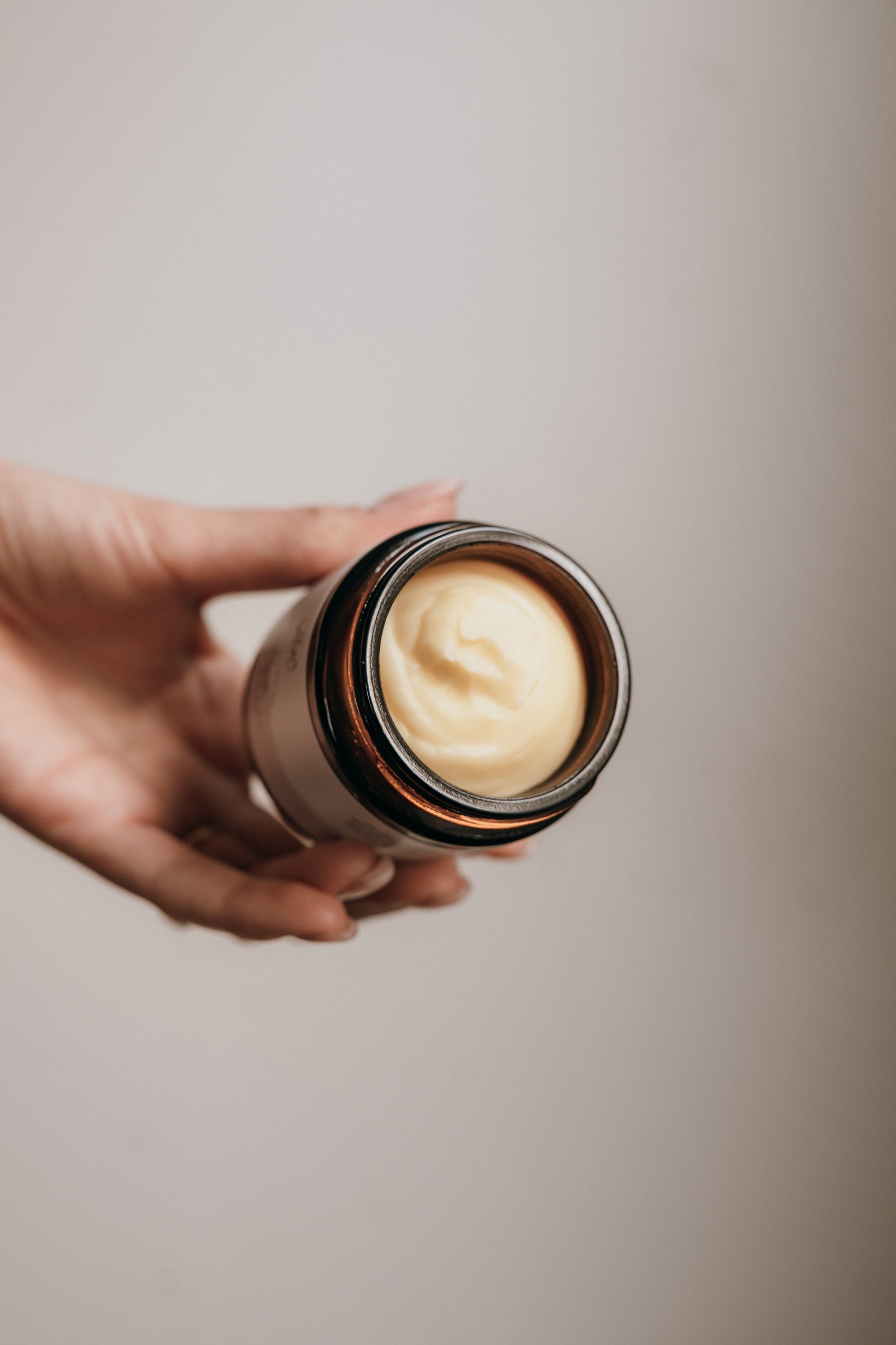 Hand holding a jar of cream against a neutral background
