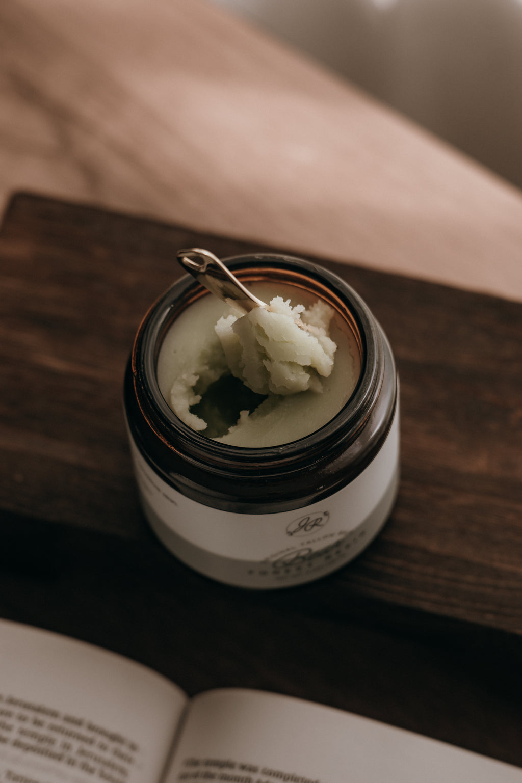 Candle in a jar with a wooden lid on a wooden surface next to an open book