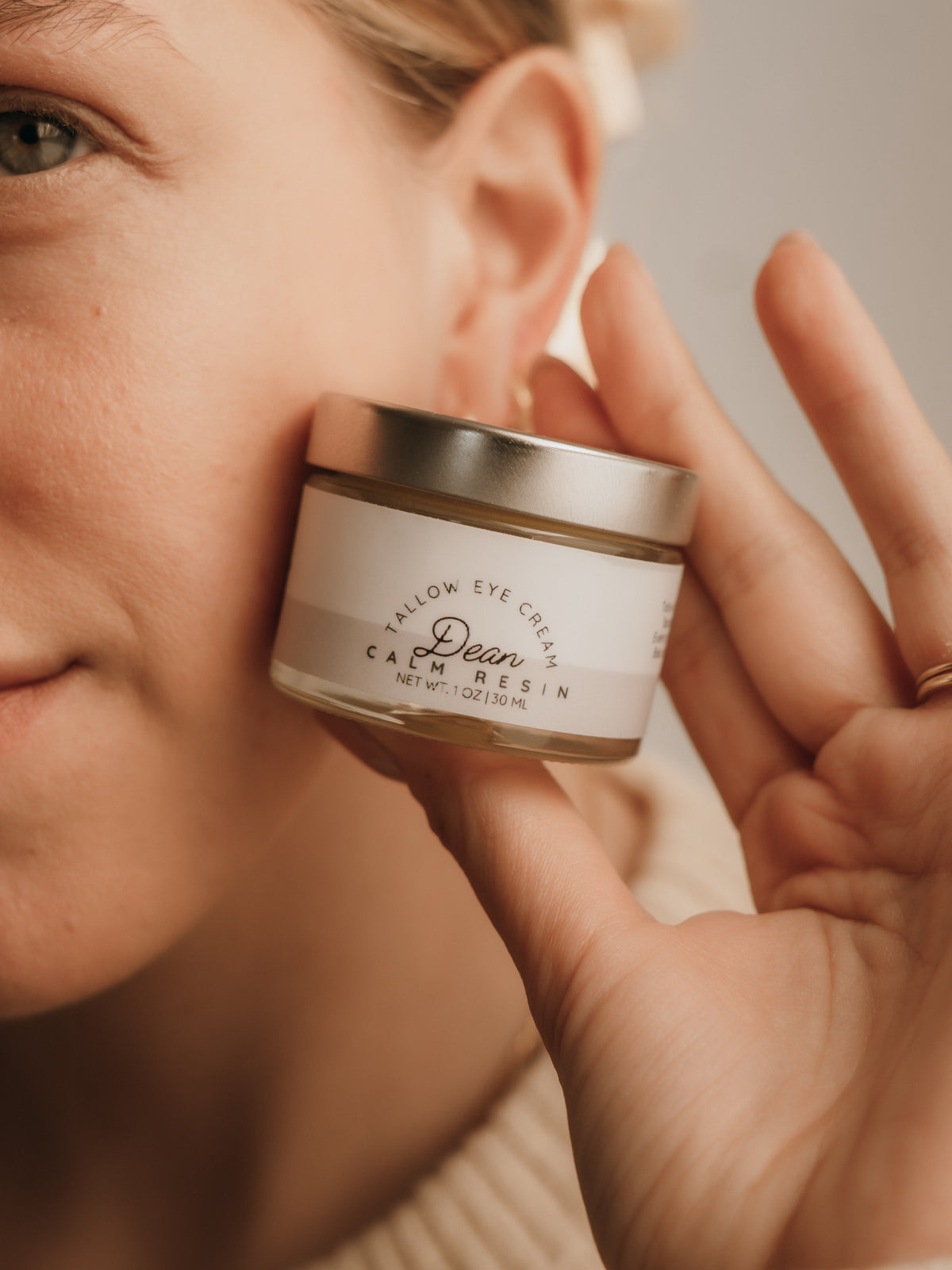 Person holding a small jar of cream close to their face