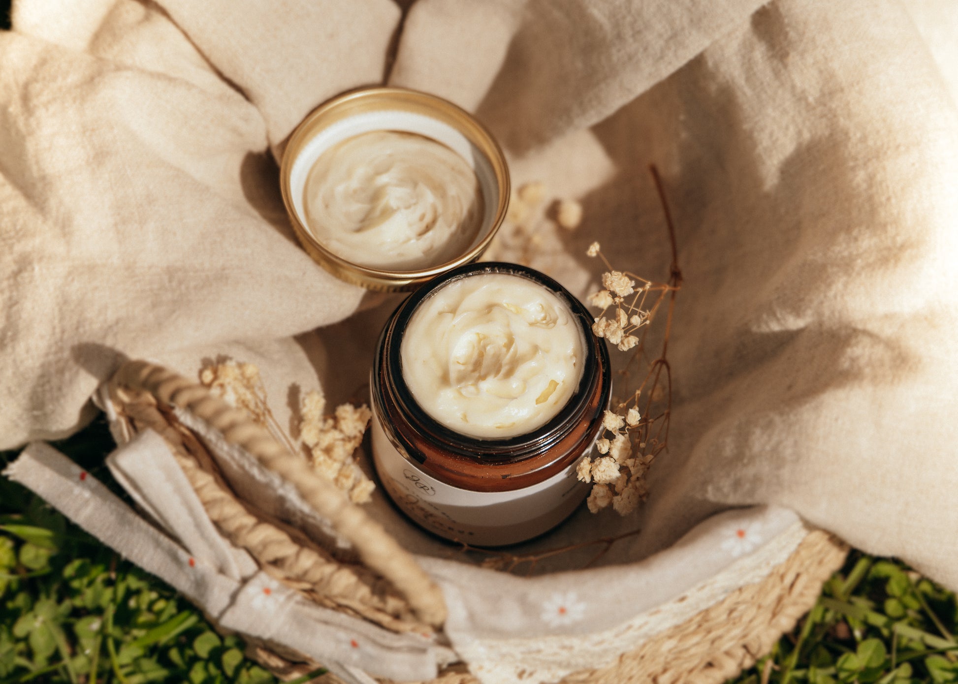 Two jars of cream on a textured surface with natural elements