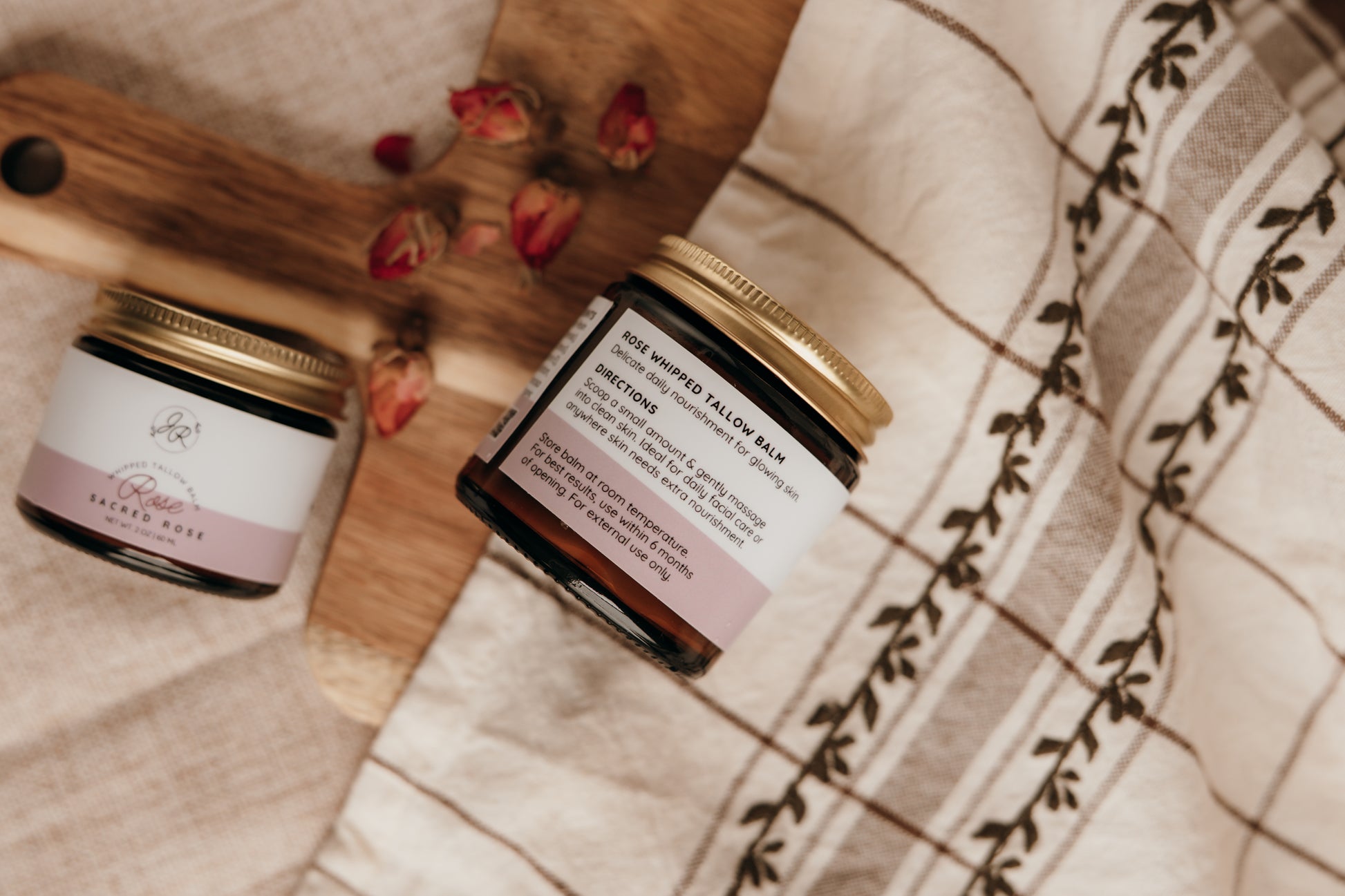 Two jars of balm on a wooden surface with a checkered cloth in the background