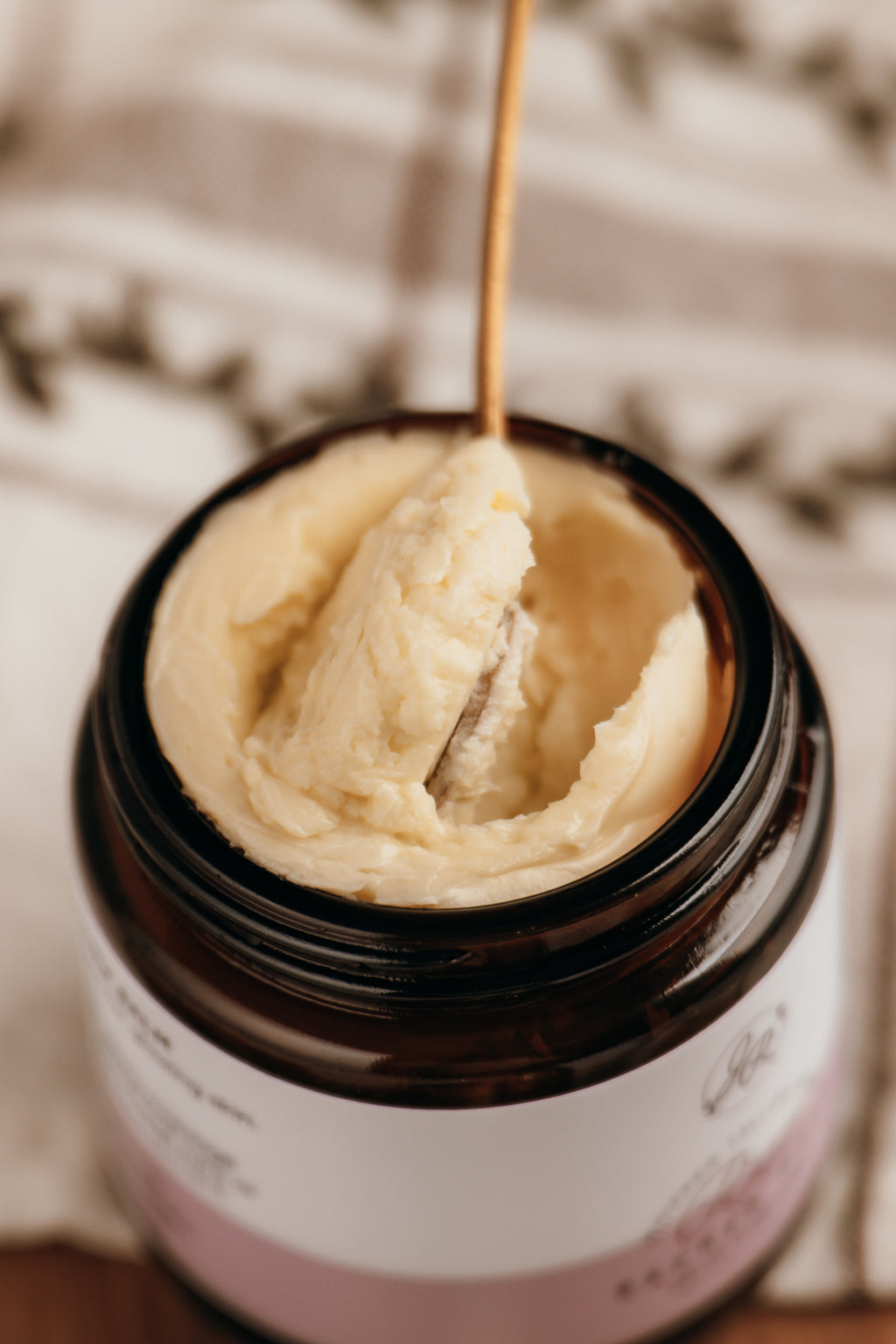 Jar of cream with a wooden spoon inside, on a textured surface.