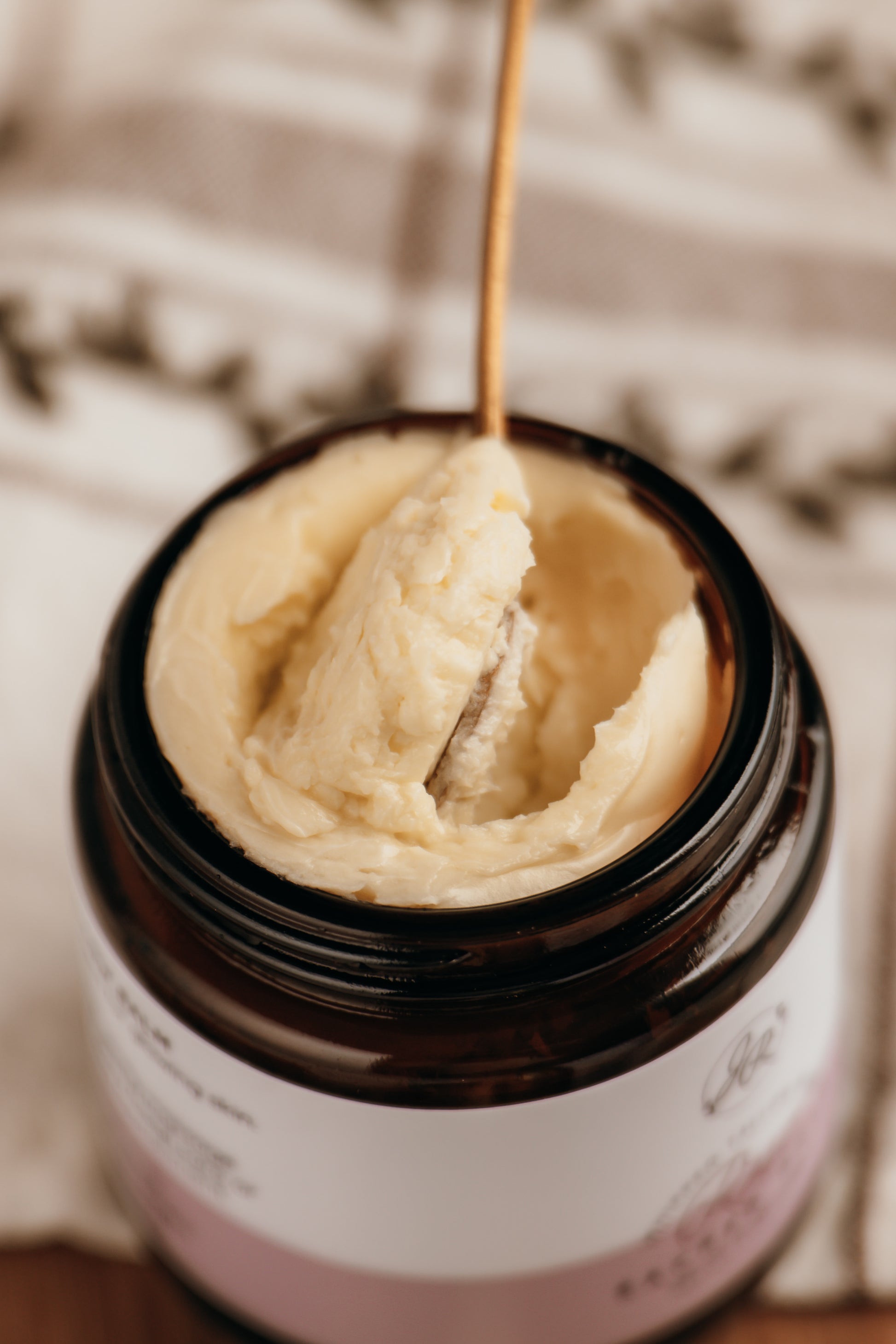 Jar of cream with a wooden spoon inside, on a textured surface.