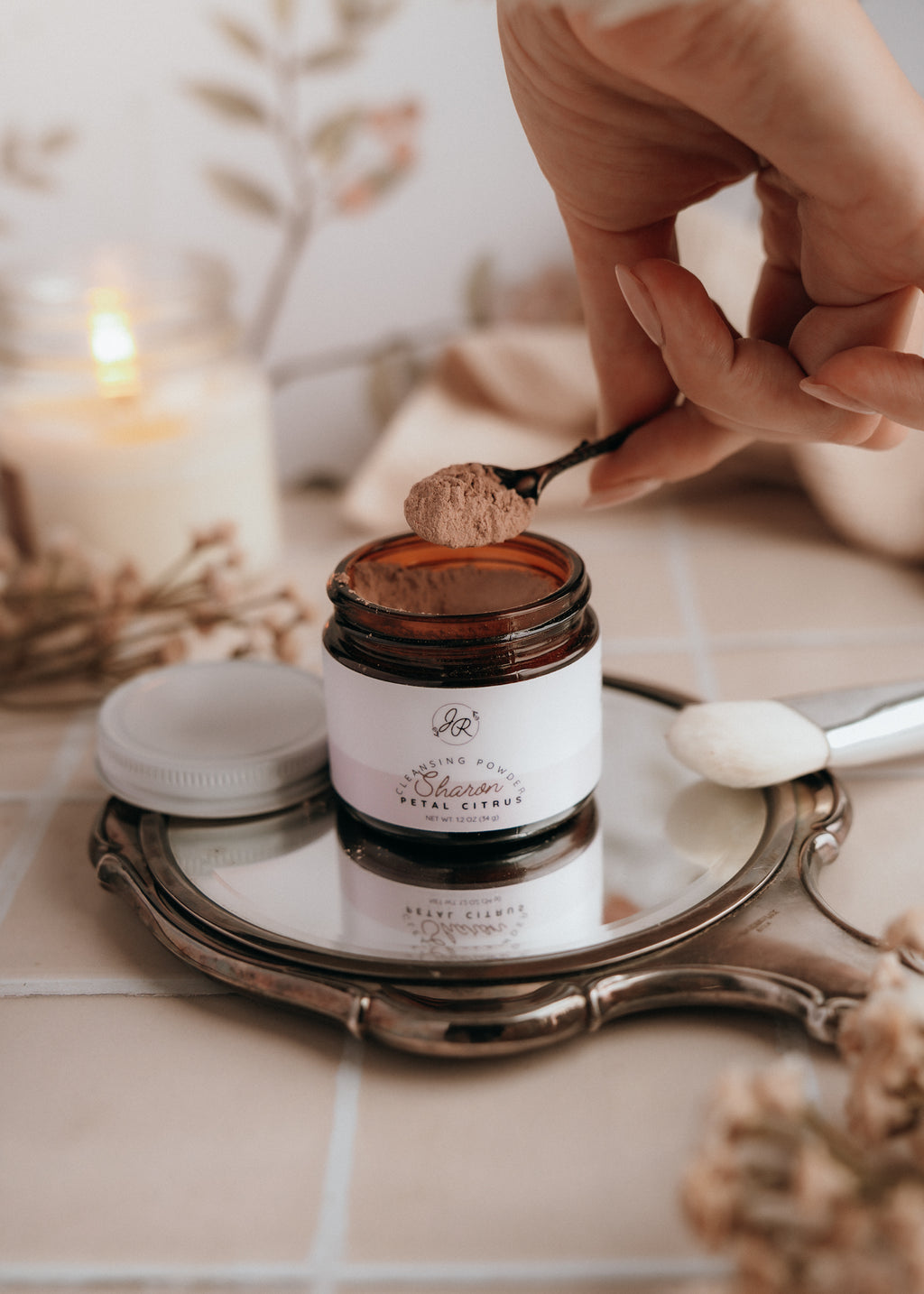 Jar of exfoliatorwith a spoonful being taken, placed on a decorative tray with a candle in the background.