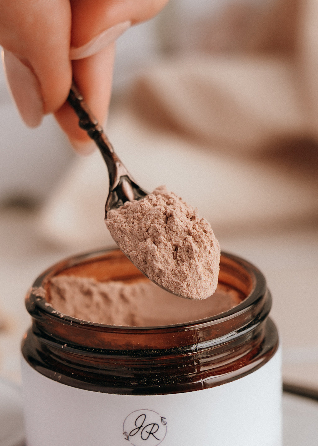 Spoonful of brown powder over a jar with a brand logo, blurred background